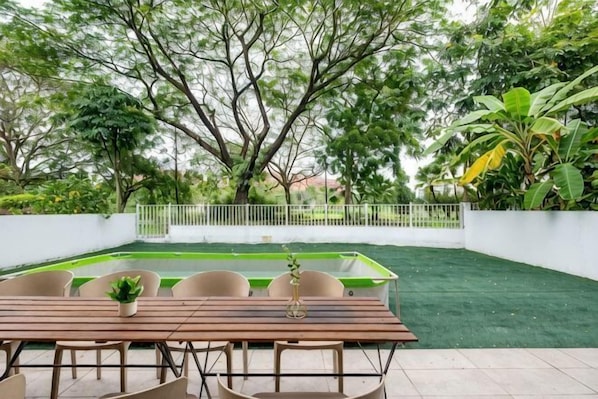 An outdoor patio with a wooden table and chairs, surrounded by greenery and a white fence.