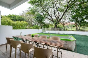 Een terras buiten met een eettafel en stoelen, omgeven door groen en een zwembad.