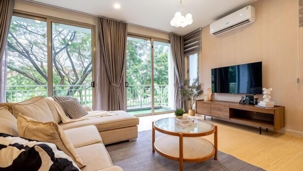 Un salon moderne avec un canapé, une table basse ronde, un téléviseur et un balcon agrémenté de rideaux.