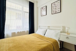 A hotel room with a bed, a nightstand, a lamp, and two framed pictures on the wall.