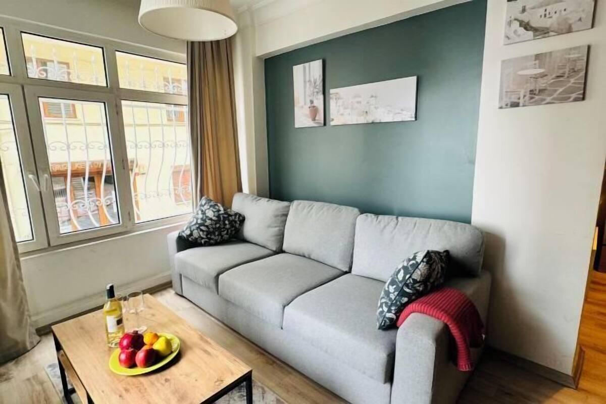 A living room with a grey sofa, a wooden coffee table with fruit, and a bottle of wine.