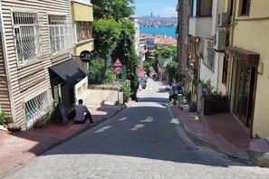 A narrow street with buildings on either side, a speed limit sign, and a view of a distant cityscape. - Duplex with a Bosphorus view (Istanbul)