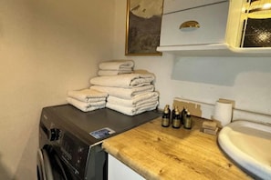 A laundry area with stacked towels, a washing machine, and bottles on a wooden counter.