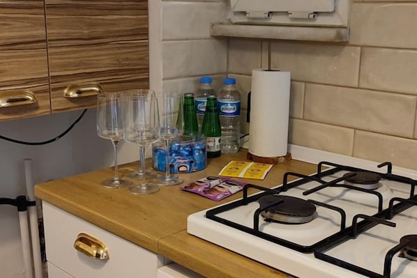 A kitchen counter with a gas stove, wine glasses, bottles, and a paper towel dispenser.