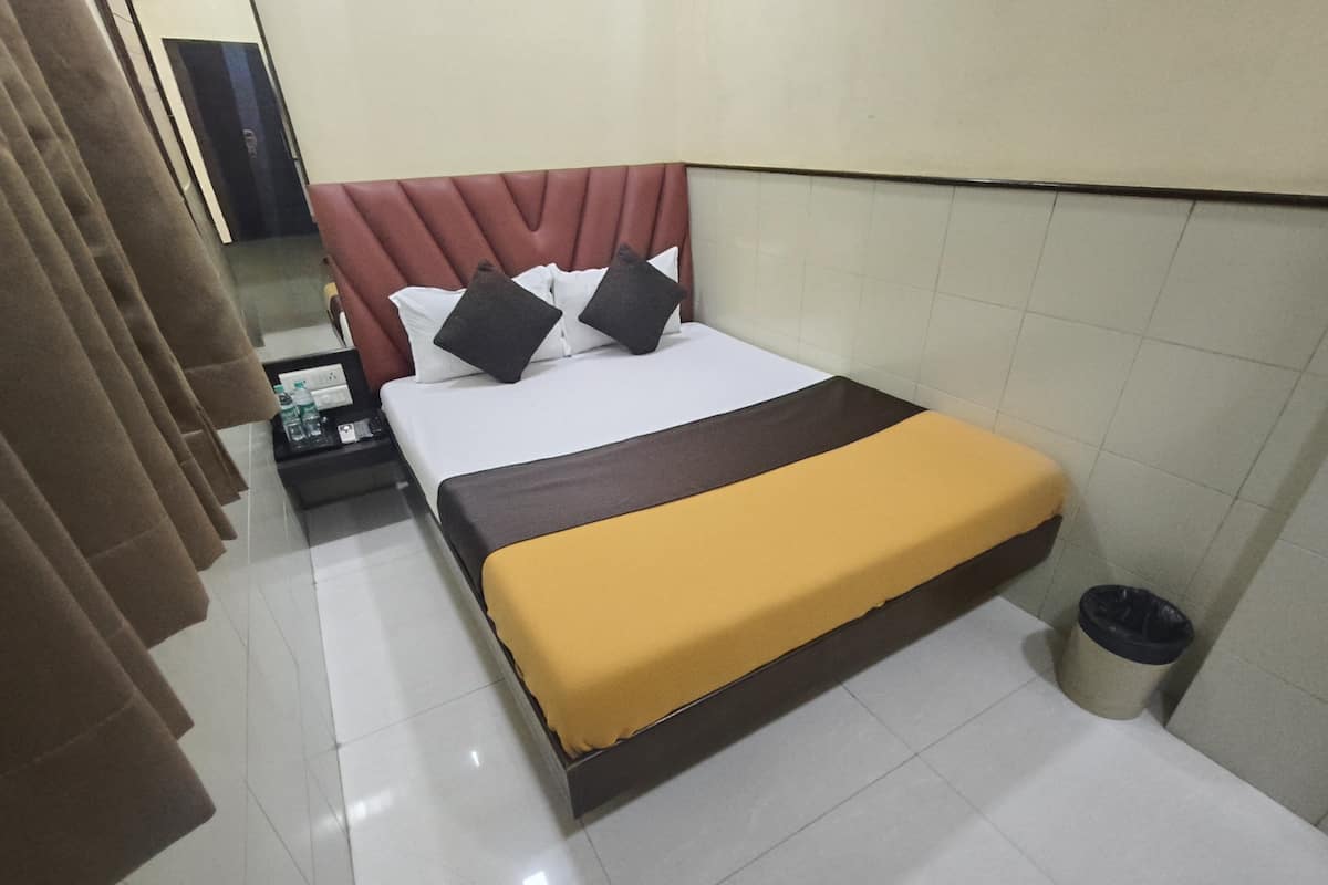 A hotel room with a bed, a nightstand, a trash bin, and a curtain.
