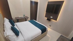 Habitación de hotel con cama, televisión montada en la pared, una mesita con una botella de agua y una puerta.