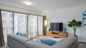 Un salon moderne avec un canapé, un téléviseur, un meuble en bois et de grandes fenêtres.