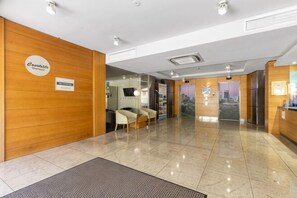 A hotel lobby with a reception desk, seating area, and a view of the cityscape through the glass wall. - Mounts Bay Stay 2 Bedroom Apt - Kings Park - Free Parking (Perth)