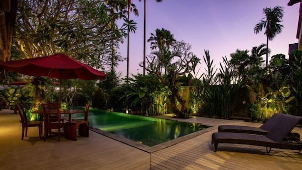A wooden deck with a pool, lounge chairs, and a dining area with a red umbrella. - Enchanting Canggu Villa (Bali)