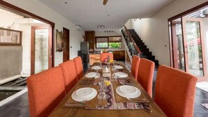 A dining area with a long table set for six, orange upholstered chairs, a ceiling fan, and a staircase leading to an upper level. - Enchanting Canggu Villa (Bali)