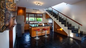 A modern kitchen with a central island, a staircase, and a view of greenery outside. - Enchanting Canggu Villa (Bali)