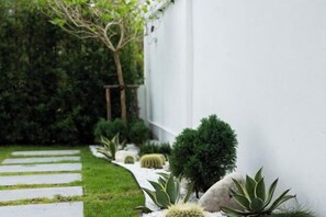 A garden with a stone pathway, various plants, and a white wall. - Prime Deluxe Villa No. V17 (Sattahip)