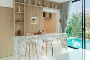 A modern kitchen with a marble countertop, wooden shelves, and a view of a swimming pool.