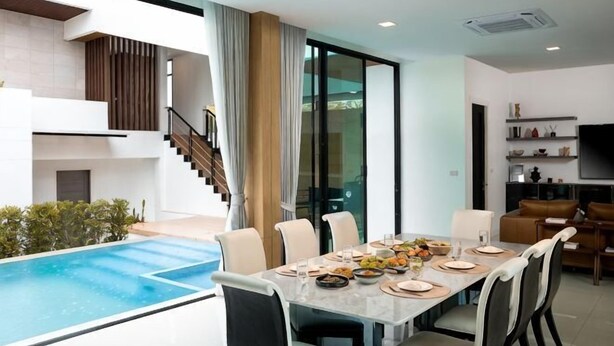A dining area with a pool view, a staircase, and a living room with a TV. - Prime Deluxe Villa No. V17 (Sattahip)