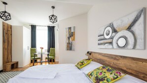 Une chambre d’hôtel dotée d’un grand lit, d’une tête de lit en bois, d’un coin repas avec une table et des chaises, et d’œuvres d’art accrochées aux murs.