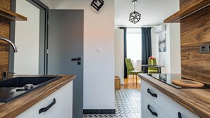 Une cuisine moderne avec un sol à motifs noir et blanc, des meubles en bois et une chaise verte à l’arrière-plan.