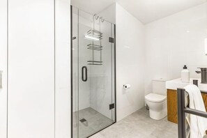 Un baño moderno con cabina de ducha de vidrio, inodoro y lavamanos con mueble de madera.
