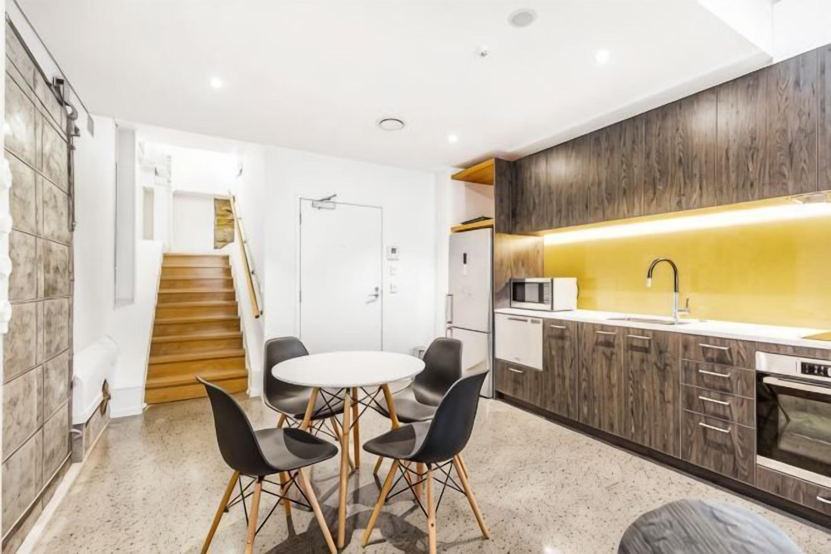 A modern kitchen with a dining area, wooden staircase, and a white door.
