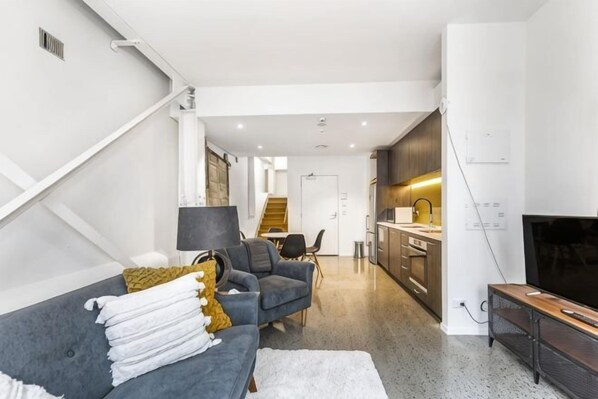 Una sala moderna con un sofá, televisión y una cocina al fondo.
