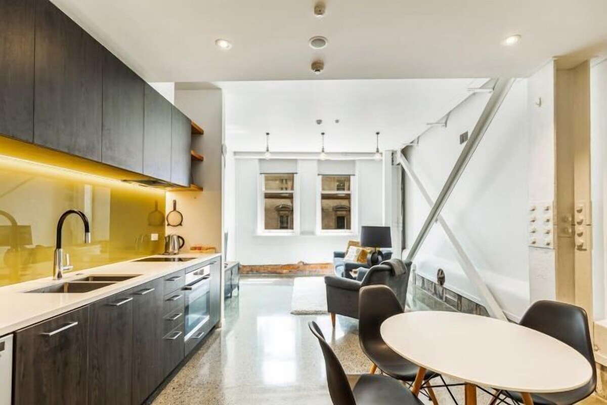 Une cuisine moderne avec des meubles de couleur sombre, un plan de travail blanc et un coin repas comprenant une table ronde et des chaises.