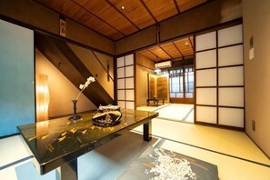 Une pièce de style japonais traditionnel, avec un sol recouvert de tatamis, une table basse ornée d’un vase et de fleurs, et des portes coulissantes.