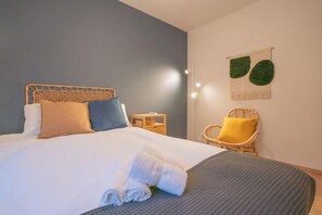 A neatly made bed with a wooden headboard, a small bedside table, and a chair with a cushion. - Travel Time Teradacho Noake (Osaka)