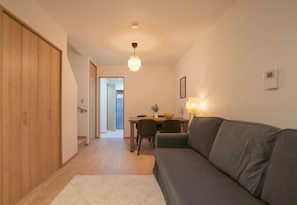 A living room with a sofa, a dining table, and a kitchen area in the background.