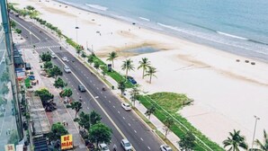 A coastal road with a beach on one side and a modern building on the other. - Beachfront 2 Bedroom Appartment with Glass wall by Villuxy (Da Nang)