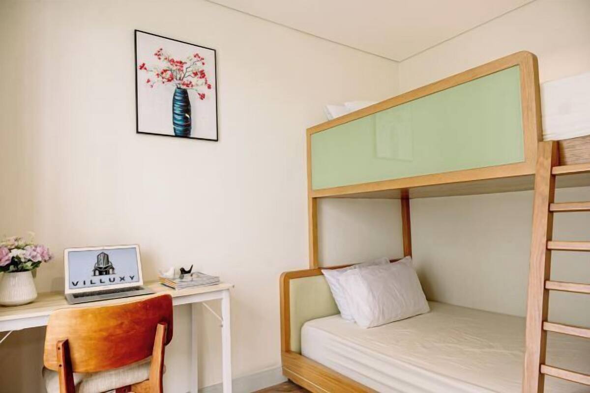 A bunk bed with a desk and chair, a laptop, and a framed picture on the wall.