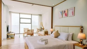 A hotel room with a large bed, a desk, a chair, and a view of the sea. - Beachfront 2 Bedroom Appartment with Glass wall by Villuxy (Da Nang)