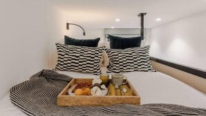 Hotellihuone, jossa on sänky, ruutukuvioiset tyynyt, tarjotinalusta aamiaistarvikkeineen ja seinään kiinnitetty valaisin.