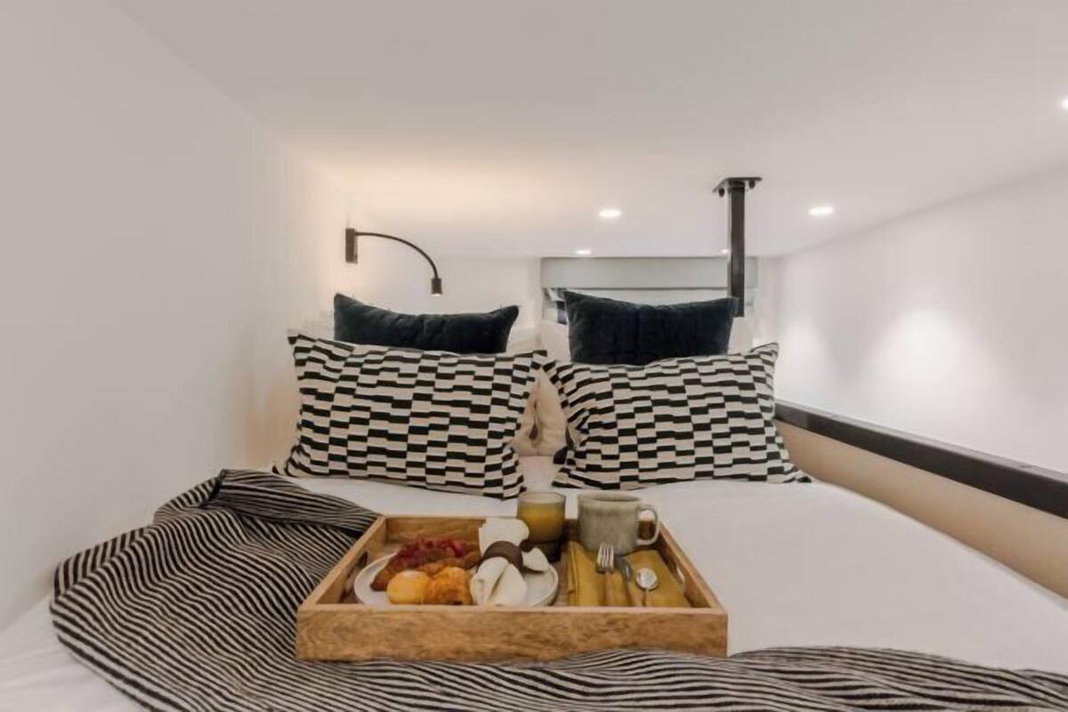 Habitació d'hotel amb llit, almoinades de quadres, safata amb elements per esmorzar i aplíc d'il·luminació fixat a la paret.