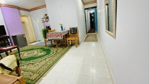 A dining area with a table and chairs, a green patterned rug, and a television. - Caesar Studio Apartment (Alexandria)