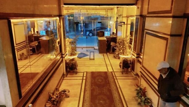 A hotel lobby with a central reception desk, a glass partition, and a view of the street outside. - Caesar Studio Apartment (Alexandria)
