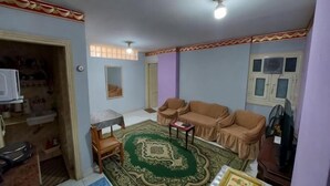 A living room with a sofa, a coffee table, a rug, and a television. - Caesar Studio Apartment (Alexandria)