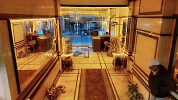 A hotel lobby with a reception desk, seating area, and a view of the street outside.