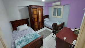 A bedroom with two beds, a wardrobe, a desk, and a chair. - Caesar Studio Apartment (Alexandria)