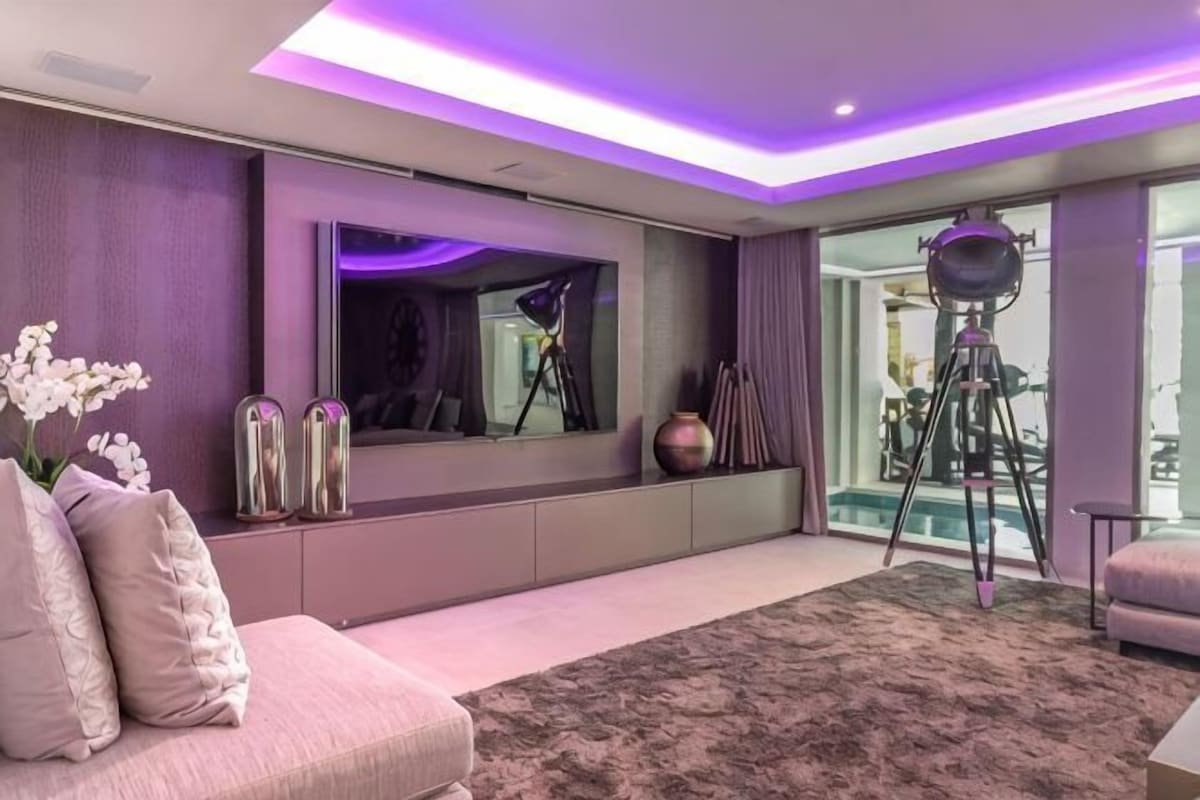 A modern living room with a sofa, a large flat-screen TV, and a tripod in the background.
