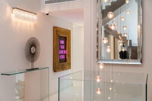 A modern interior with a glass staircase, a neon sign, and a large mirror reflecting the staircase. - All About Villa Serenity (Marbella)