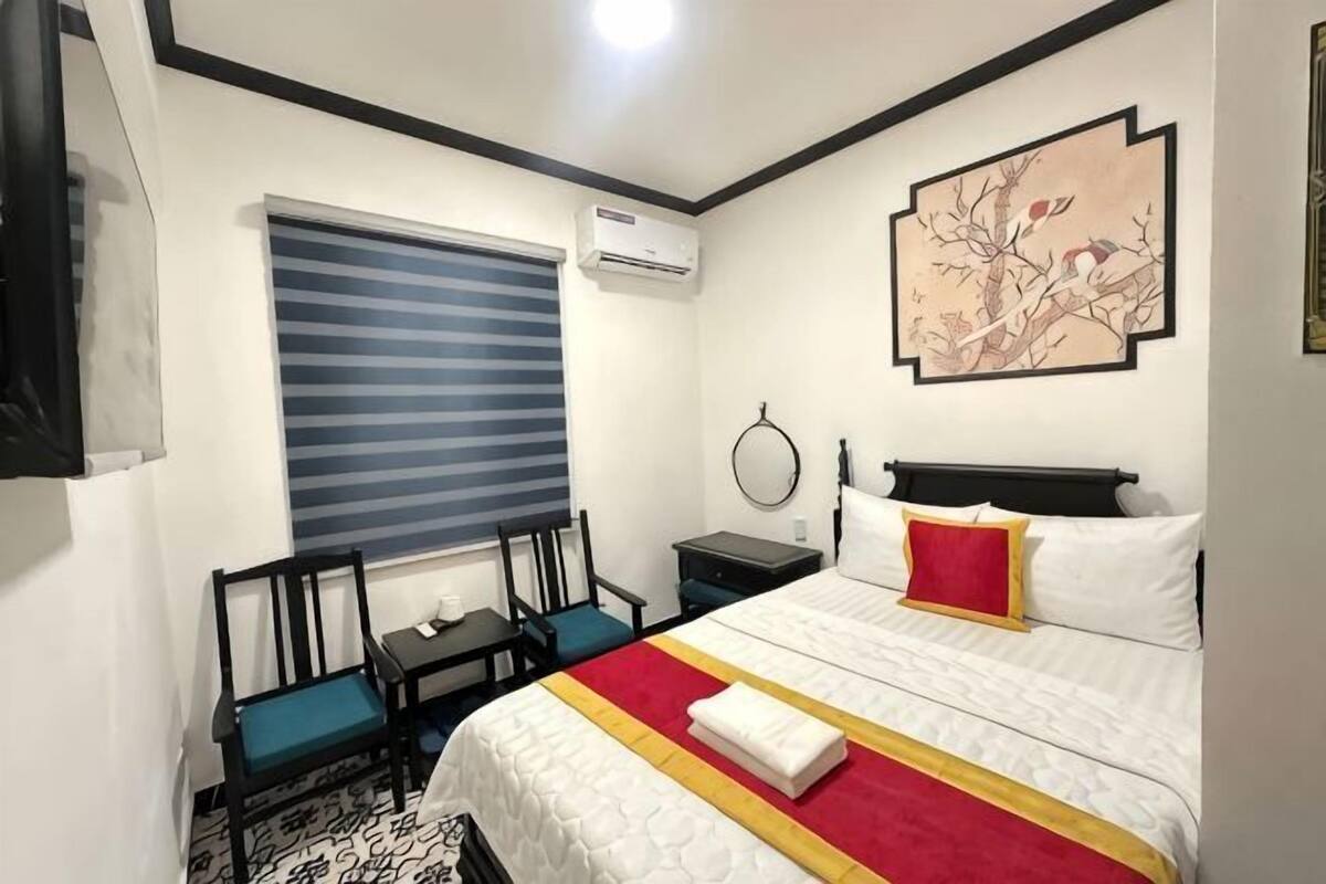 Ein Hotelzimmer mit Bett, Schreibtisch, Stuhl, einem Fenster mit Jalousien und einer Wand-Klimaanlage.
