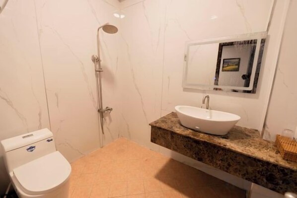 A bathroom with a shower, toilet, sink, and marble walls.
