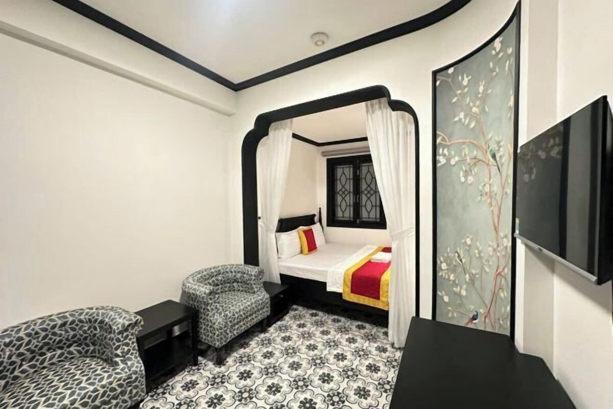A bedroom with a bed, a chair, a bedside table, and a TV.