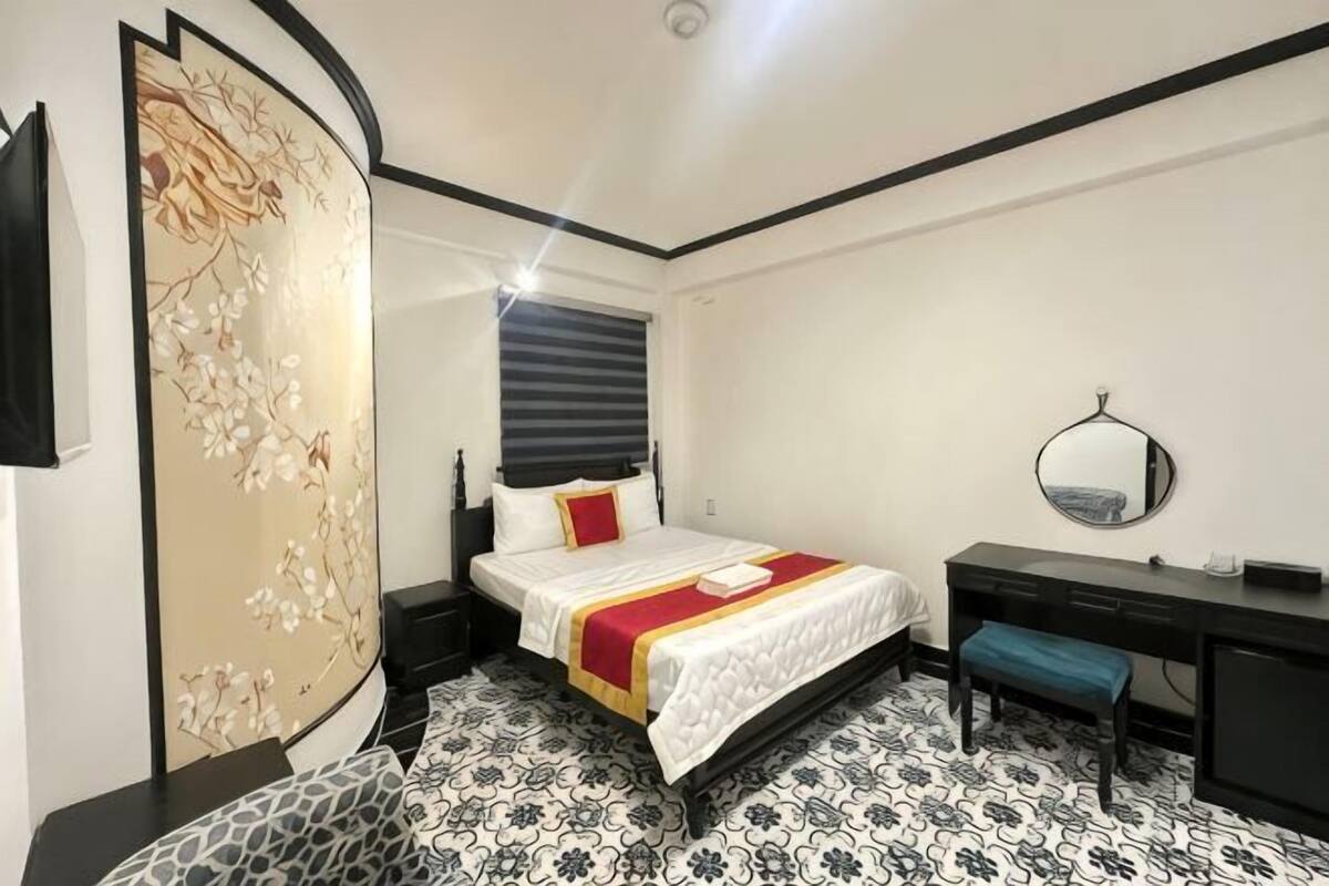 Ein Schlafzimmer mit Bett, Nachttisch, Schreibtisch, Stuhl und einem dekorativen Raumteiler.