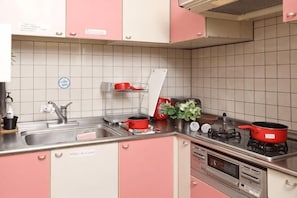 Ett kök med rosa skåp, en diskho i rostfritt stål och en röd kastrull på spisen.