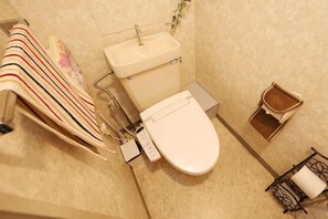 Casa de banho com sanita, lavatório, suporte para toalhas e um pequeno contentor de lixo.