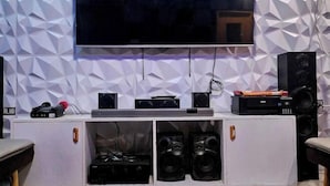 Una sala moderna con un televisor de pantalla plana montado en una pared con diseño geométrico, un mueble blanco para equipo de sonido con altavoces y una mesita.
