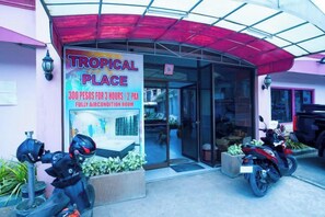 Eingangsbereich des Hotels Tropical Place mit einem Schild, einer überdachten Einfahrt und zwei draußen abgestellten Motorrädern.