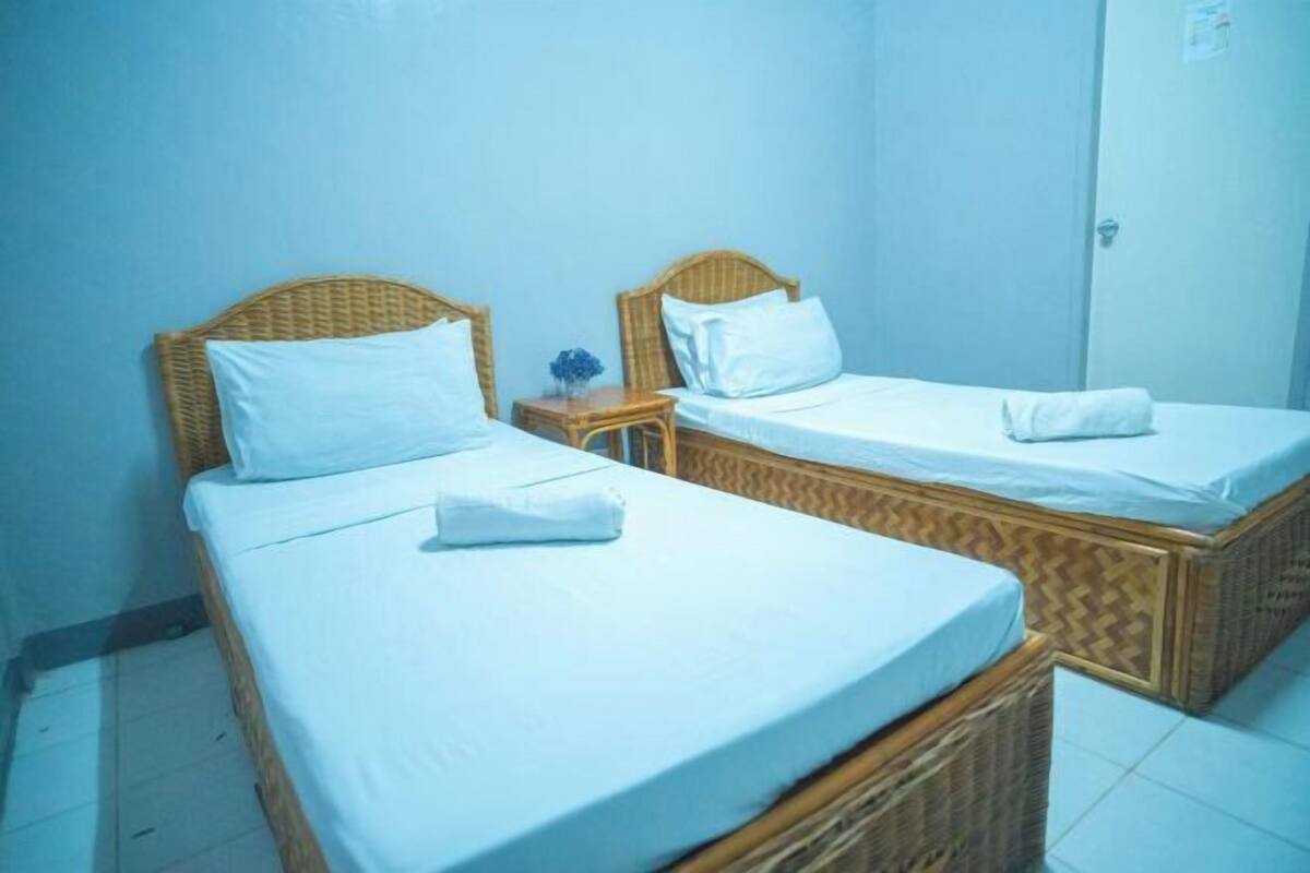 Zwei Einzelbetten mit Holz-Kopfteilen in einem Zimmer mit Fliesenboden und einer Tür.
