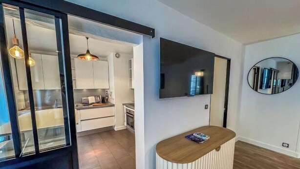 Un salon moderne avec un comptoir d’accueil en bois, un téléviseur fixé au mur et un grand miroir sur le mur.