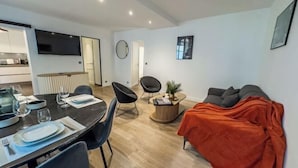 Un salon moderne comprenant un coin repas, un canapé et un téléviseur fixé au mur.